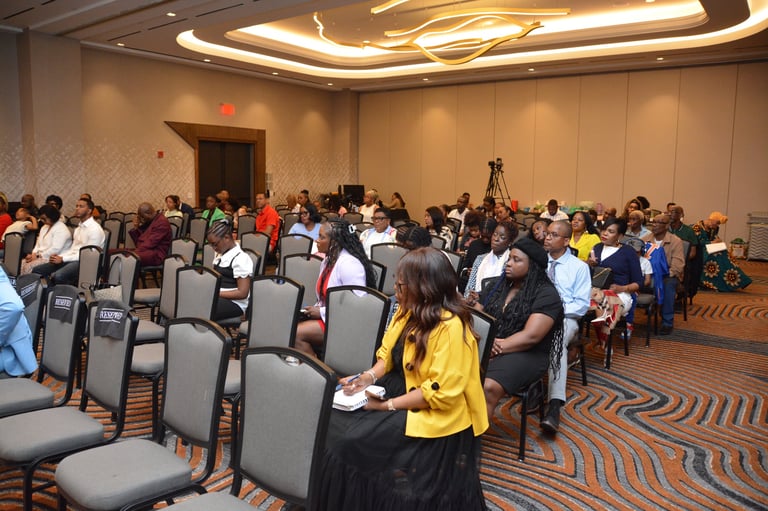 Large group of diverse attendees gathering in a hotel conference room with rows of gray chairs and modern ceiling lighting