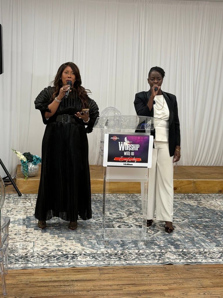 Two women speaking at a worship event on a stage with a podium and backdrop