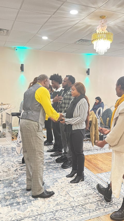 Group of people in business attire greeting and conversing at an indoor event space with turquoise accent lighting and a crystal chandelier