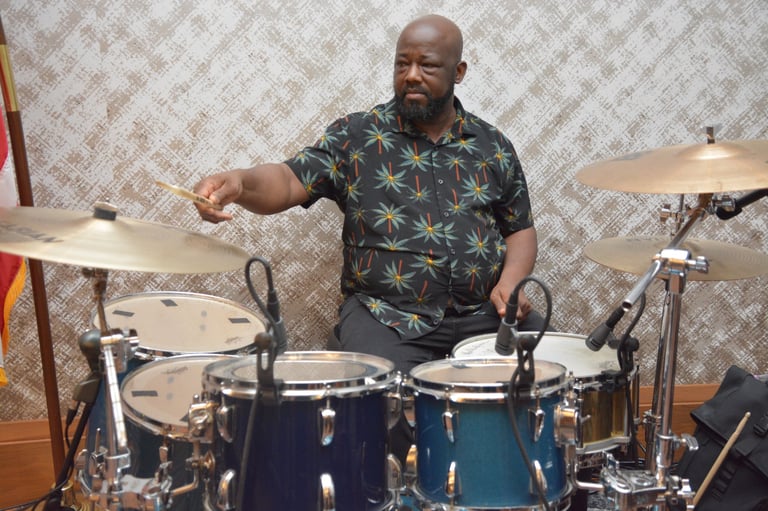 A man playing drums in a patterned shirt, with cymbals visible in a studio setting