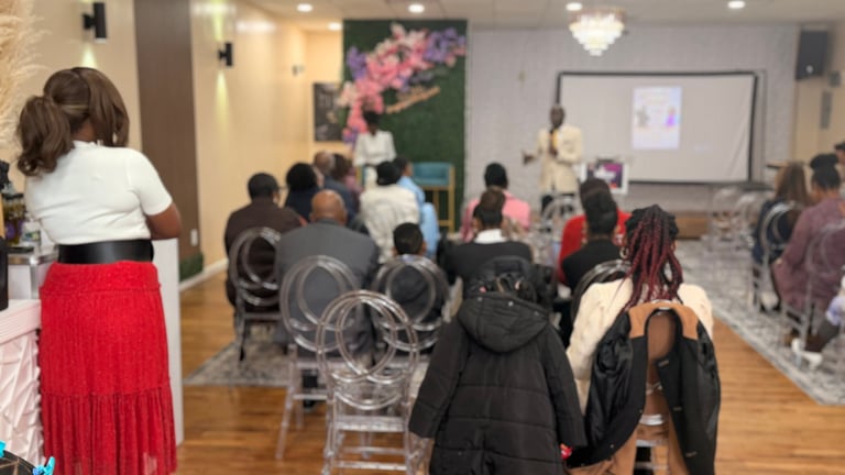 Group of people seated and standing in an indoor venue attending a presentation or event with displayed artwork on the walls