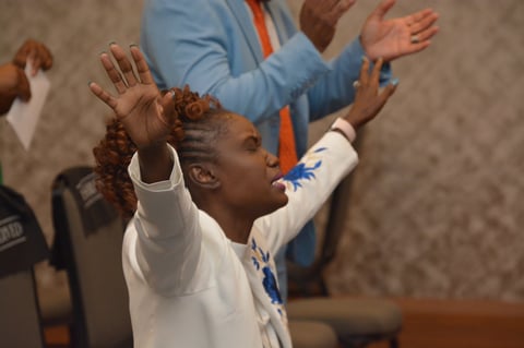 Young child in white shirt with raised arms engaging in indoor activity with adults in casual clothing nearby