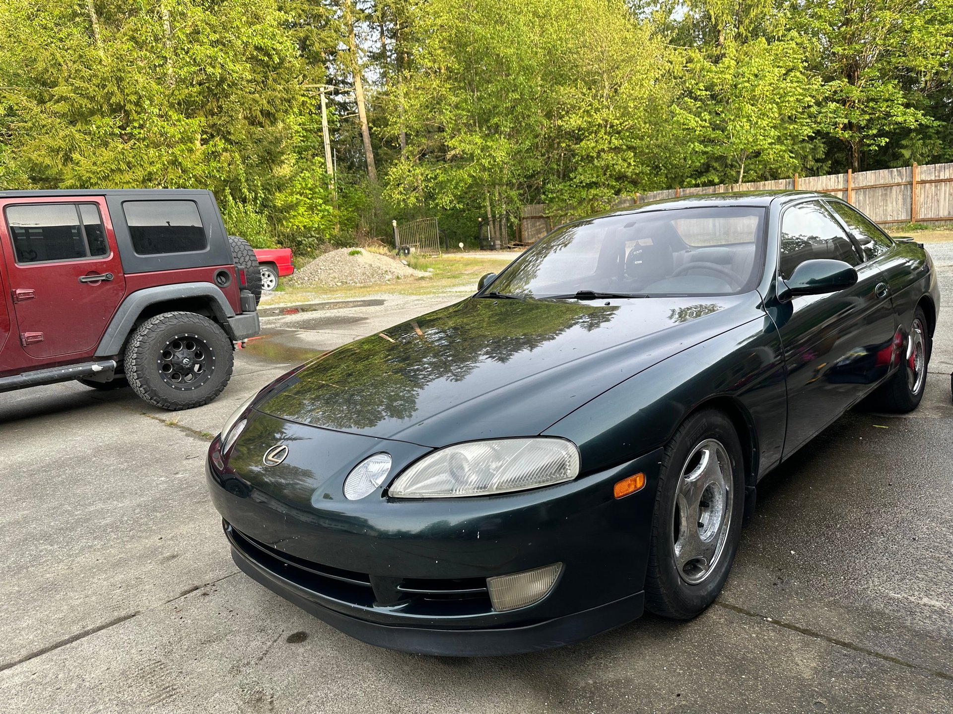 Black sports coupe parked in lot with red SUV and trees in background