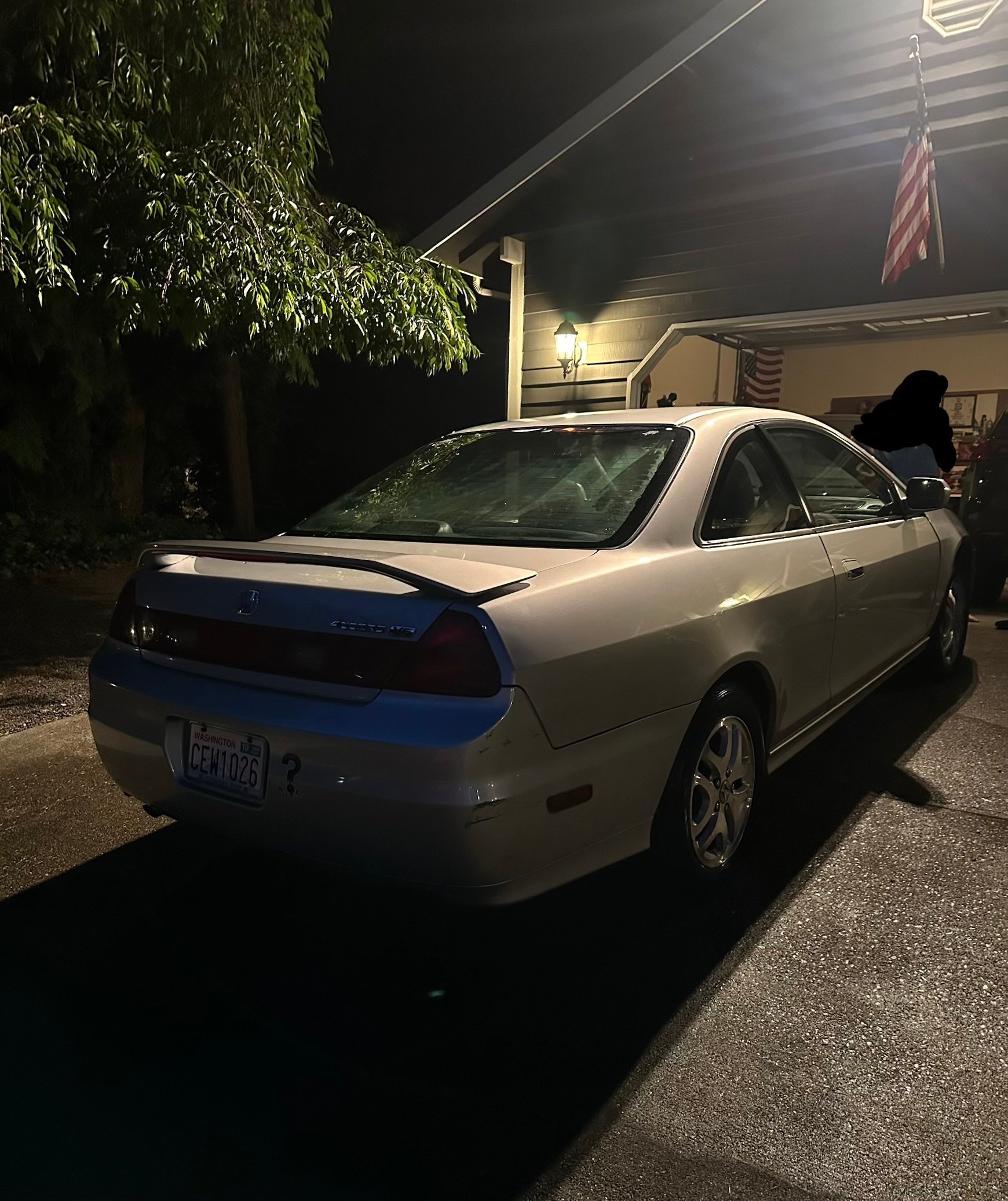 White sedan parked in driveway at night with house and garage in background