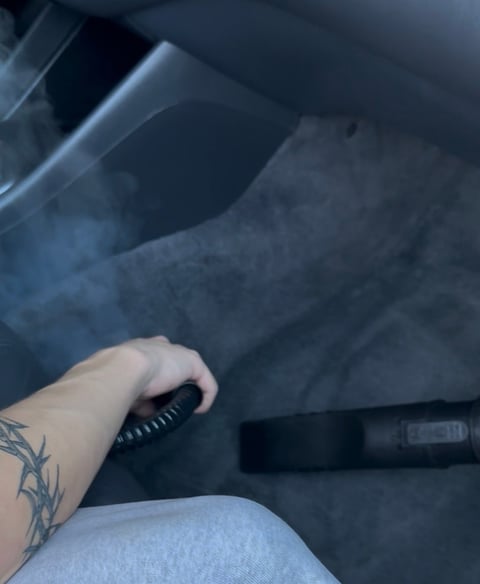 Persons tattooed hand holding a car door handle inside a vehicle with gray upholstery