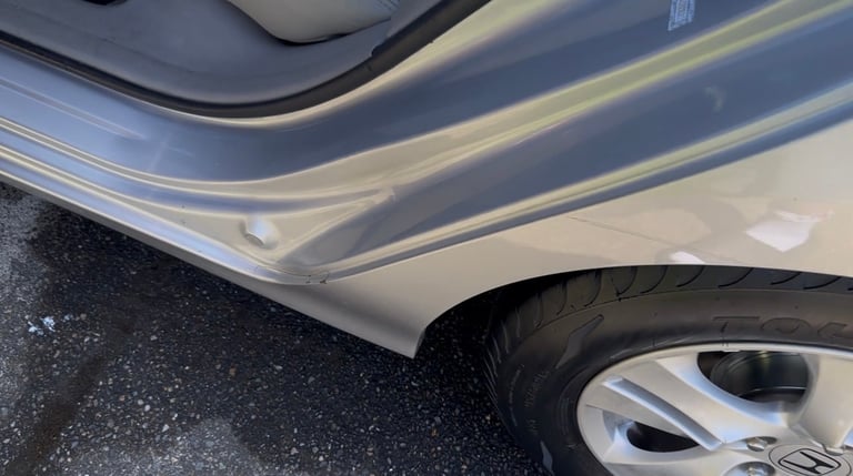 Close-up of white car door with blue stripe trim and black tire visible on asphalt
