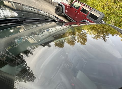 Red Hummer H2 parked on rural road with green foliage and water reflection visible