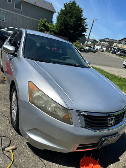 Silver Honda sedan parked on residential street with headlights on and yellow charging cable visible