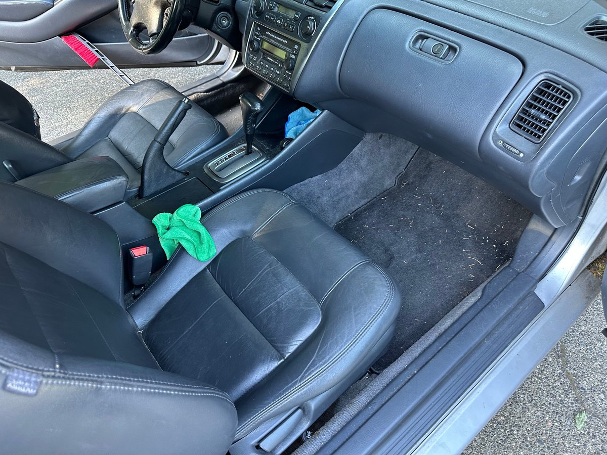 Interior of a car with black leather seats showing wear, dashboard, and a green cloth on the center console