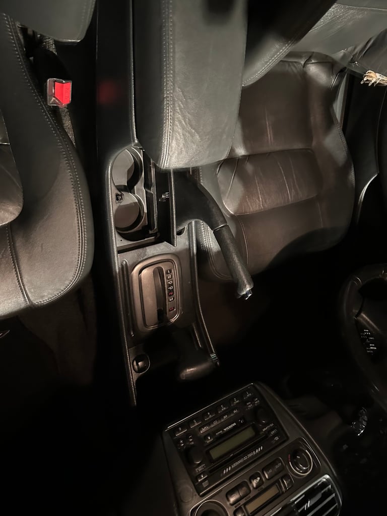 Car interior showing center console with automatic transmission shifter, cup holder, and black leather seats