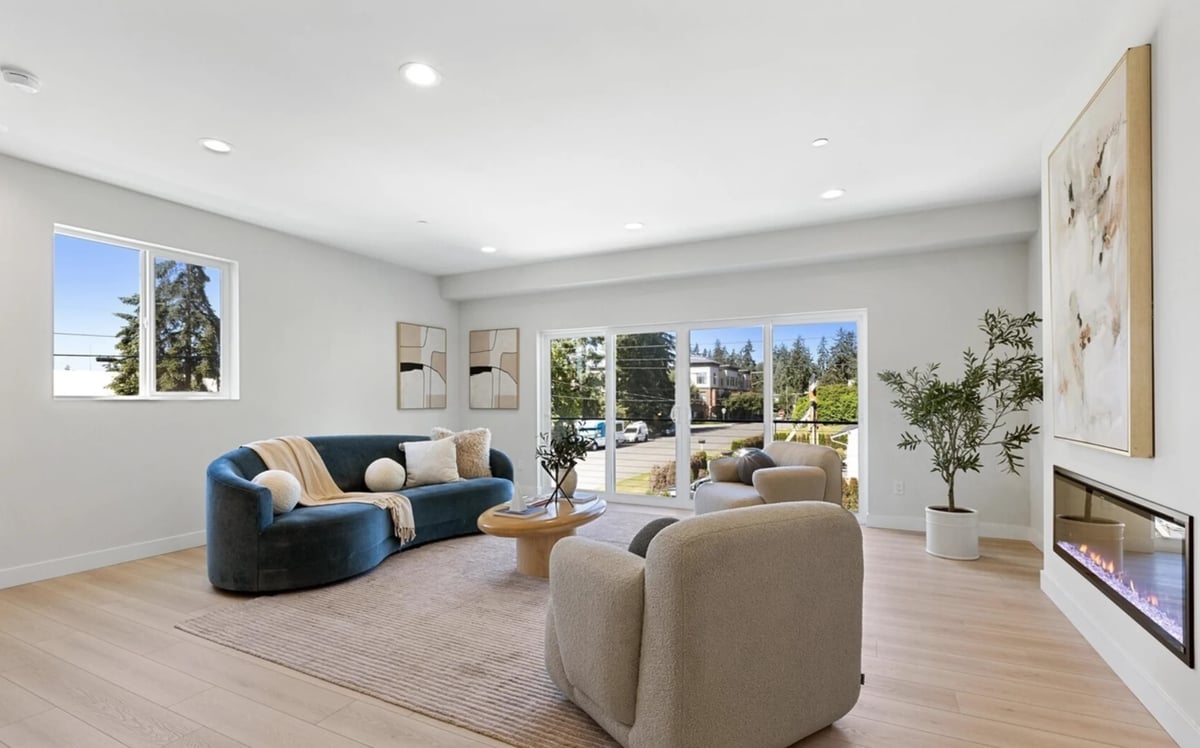 Modern living room with blue curved sofa, beige armchair, wooden furniture, large windows with mountain views, and fireplace