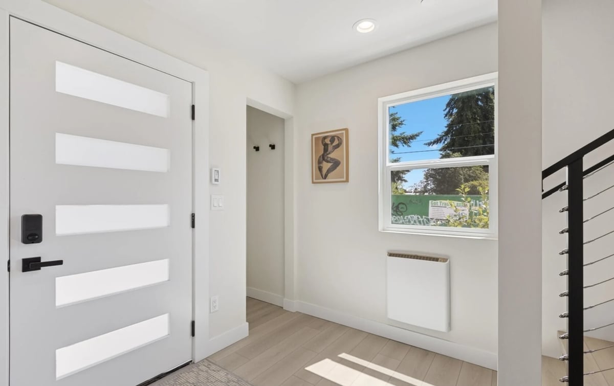 Modern entryway with white horizontal striped door, light wood floor, window overlooking outdoor view, and metal stair railing