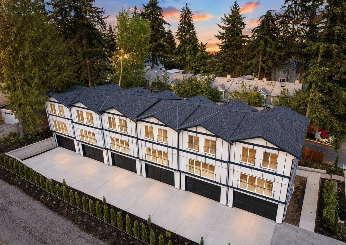 Aerial view of modern three-unit townhomes with dark roofs and contemporary architecture surrounded by evergreen trees at dusk