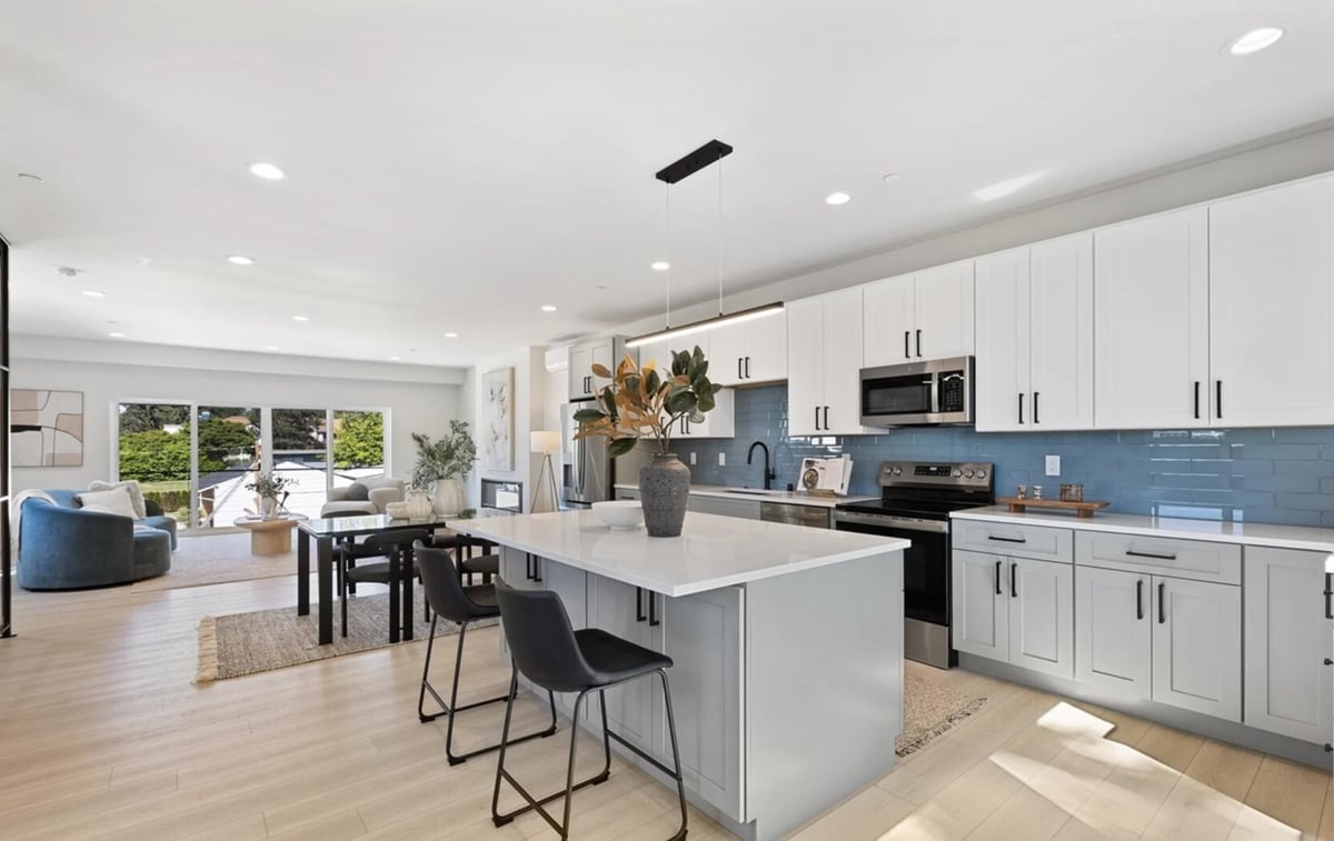 Modern open-concept kitchen with white cabinetry, blue tile backsplash, white island with black seating