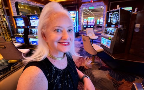 Woman with white hair smiling at camera in a casino surrounded by colorful slot machines