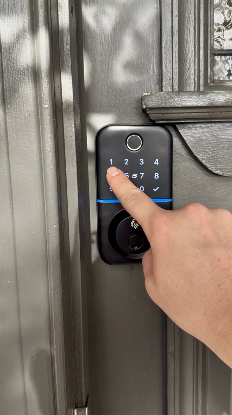 Person entering code on a black digital keypad lock mounted on a gray metal door frame