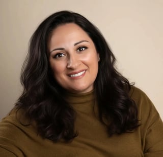 Portrait of a smiling woman with long dark wavy hair wearing an olive-brown turtleneck against a neutral beige background