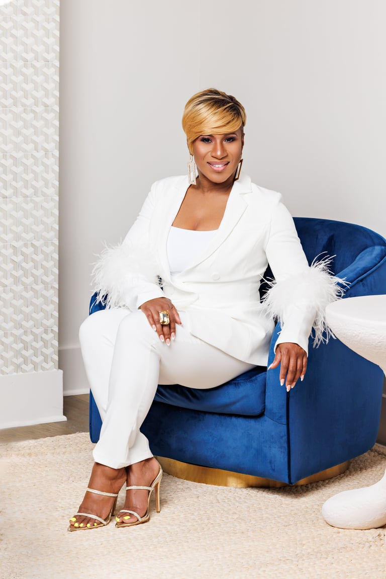 Woman in white blazer and pants with feathered cuffs sitting on a blue velvet armchair