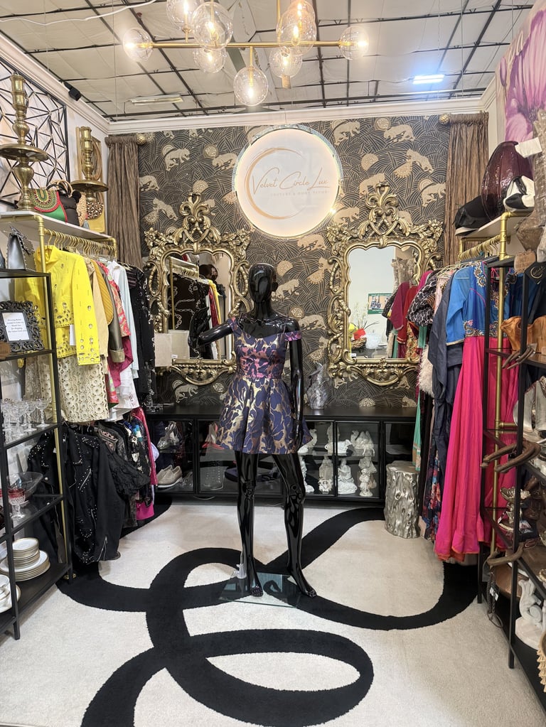 Upscale boutique clothing store interior with mannequins displaying dresses, ornate gold wallpaper, pendant lighting, and designer accessories