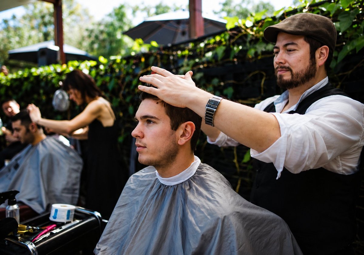 Barber styling a clients hair in an outdoor garden setting with other people in the background