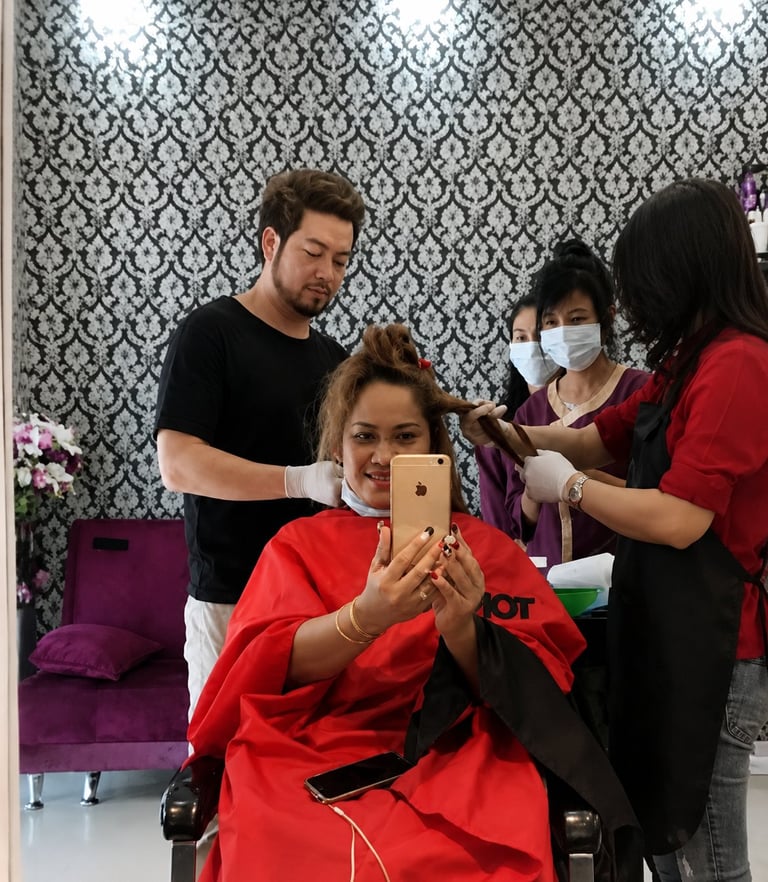 Woman in red dress taking selfie while getting hair styled by male stylist and two female staff members with ornate wallpaper background