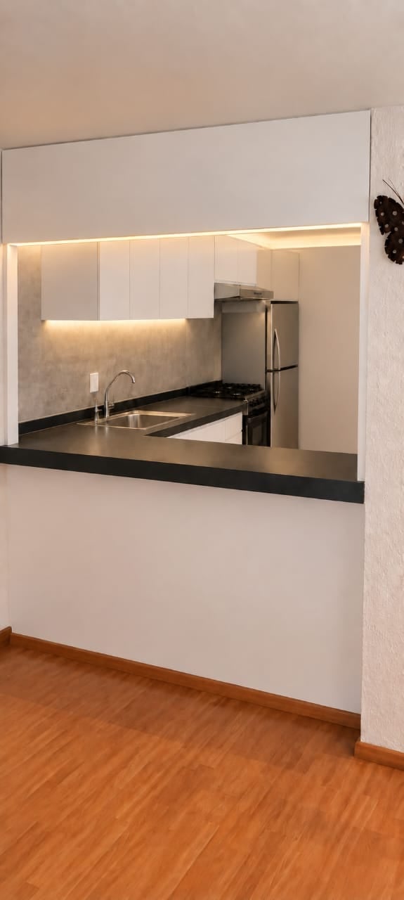 Modern minimalist kitchen with white cabinets, black countertop, stainless steel appliances, and ambient under-cabinet lighting