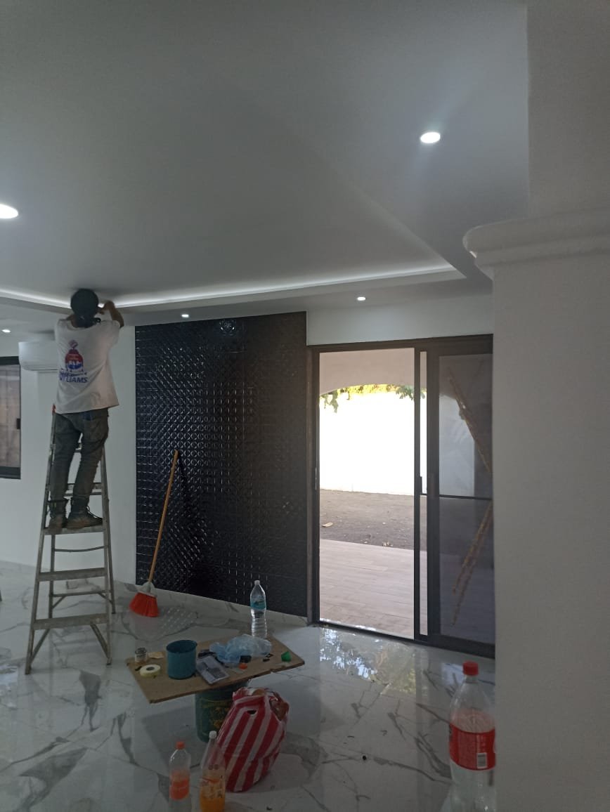 Construction worker on ladder installing black tile wall in modern home interior with glass sliding doors and white ceiling