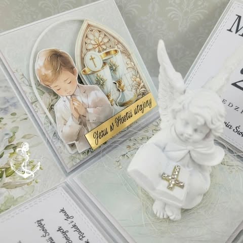 Religious christening or baptism decoration featuring a praying child icon, decorative cross, white flowers, and baptism cards on an ornamental surface.