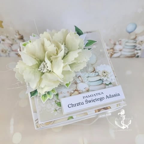 White flower arrangement card with cream peonies, babys breath, and a Polish greeting message on a decorative base