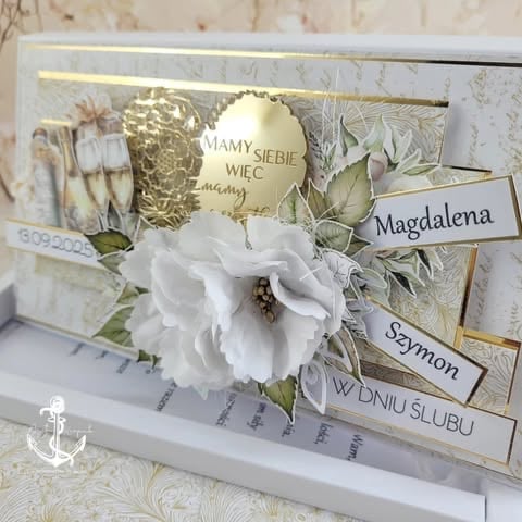 Decorative white floral card with gold accents, biblical names including Magdalena and Szymon, featuring a white flower and pressed botanicals.