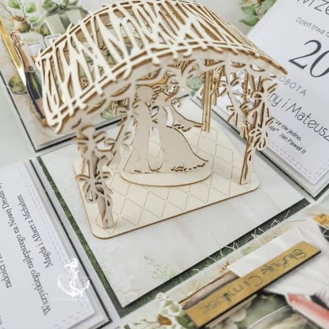 Wooden laser-cut architectural model of a house with decorative details, displayed on a white surface among papers and design materials.