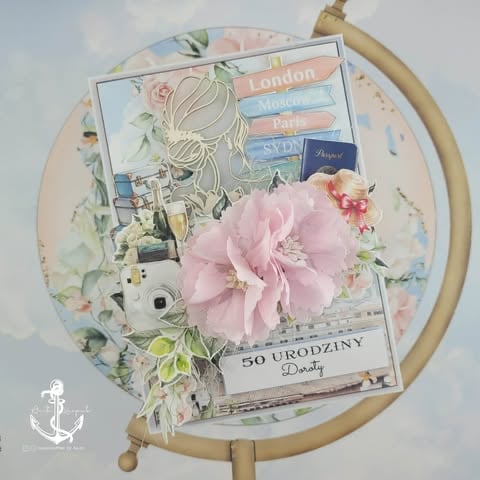 Decorative scrapbook layout on wooden hoop with travel theme, pink flower, vintage photos, and handwritten elements.