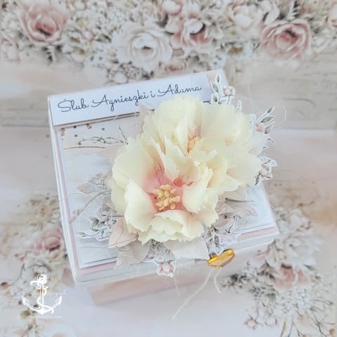 Cream peony flower resting on white decorative cards surrounded by blush and white floral arrangement