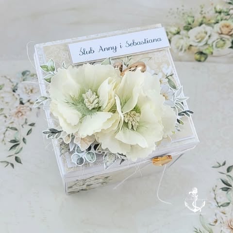 Clear acrylic box with white flowers and a name card labeled Stub Anny Sebastiana, displayed on a patterned surface