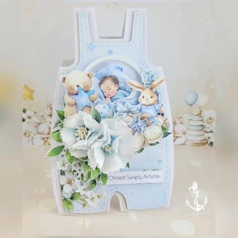 Decorative baby sleeping bag shaped card with newborn illustration, white flowers, teddy bears, and blue accents for baptism or christening