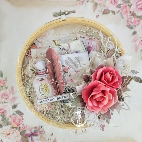 Woven basket embroidery hoop filled with pink 3D rose, feathers, decorative scissors, perfume bottle, book page, and 'Słuchaj serca' text on floral background