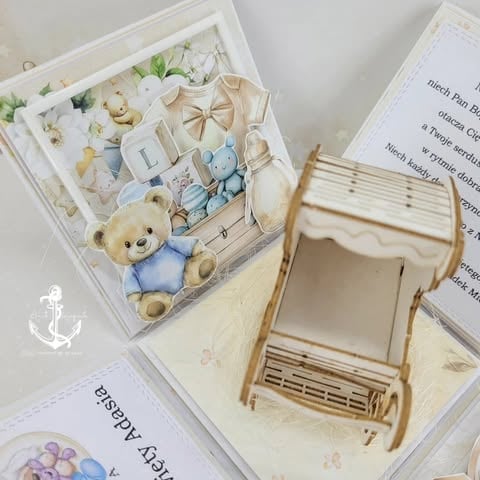 Flat lay of baby themed scrapbook elements including teddy bear, wooden cutouts, flowers, and a decorative pram on cream backgrounds