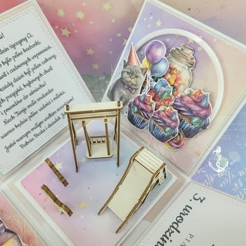 Overhead view of open book with miniature furniture, cat birthday die-cut, and open pages with text on pastel background