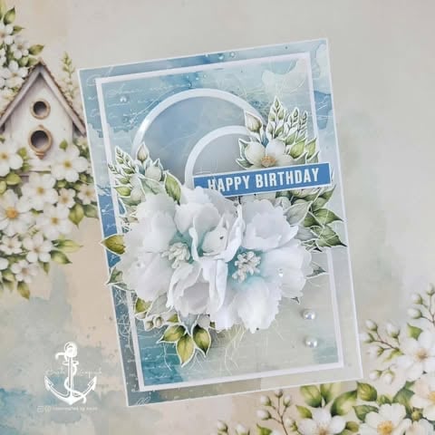 Handmade birthday greeting card with white flowers, blue watercolor background, and Happy Birthday banner surrounded by small floral accents