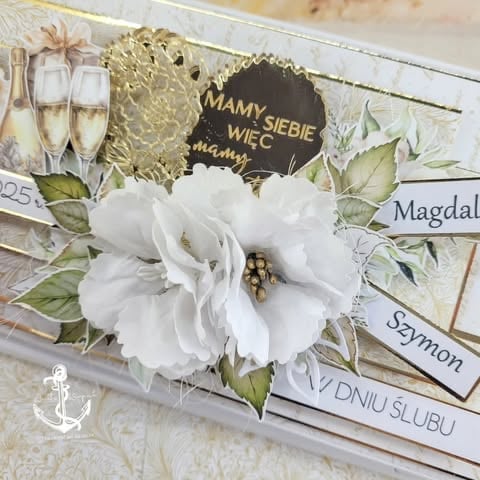 Elegant white wedding invitation with white fabric flower, champagne glasses, gold accents, and Polish text wishing newlyweds well.