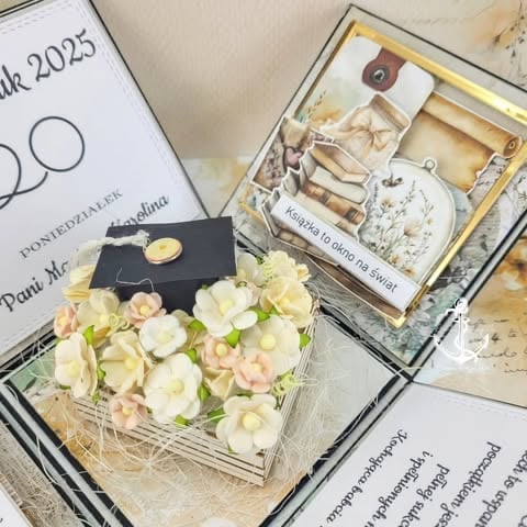 Graduation gift set with cream and pink flowers in clear box, black mortarboard cap, and spa products in wooden gift box on documents