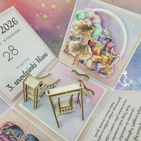 Flat lay of scrapbooking supplies including a 2028 calendar page, illustrated girl sticker with colorful gifts, miniature wooden furniture, and book pages with pink and pastel decorative elements