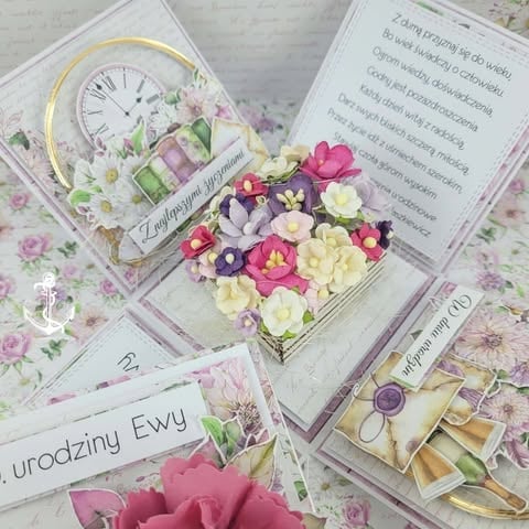 Flat lay of birthday greeting cards with colorful flowers, decorative clock, pink roses, and wrapped gifts on floral background