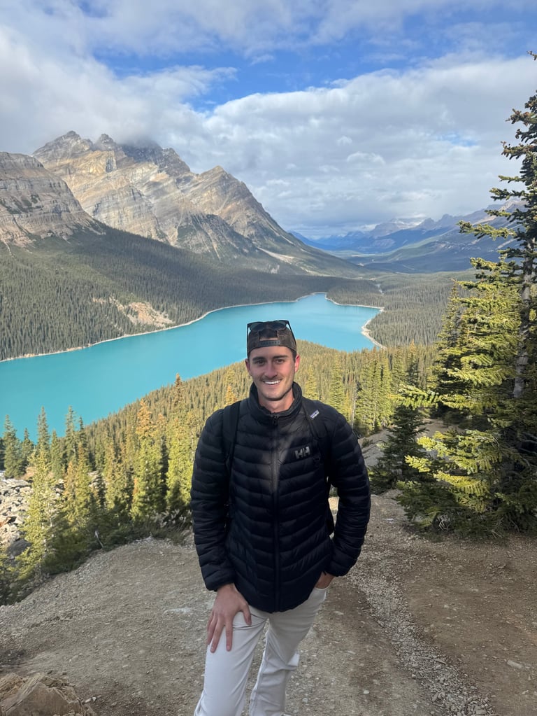 Andrew Donohue on a mountain trail overlooking a turquoise lake with snow-capped peaks