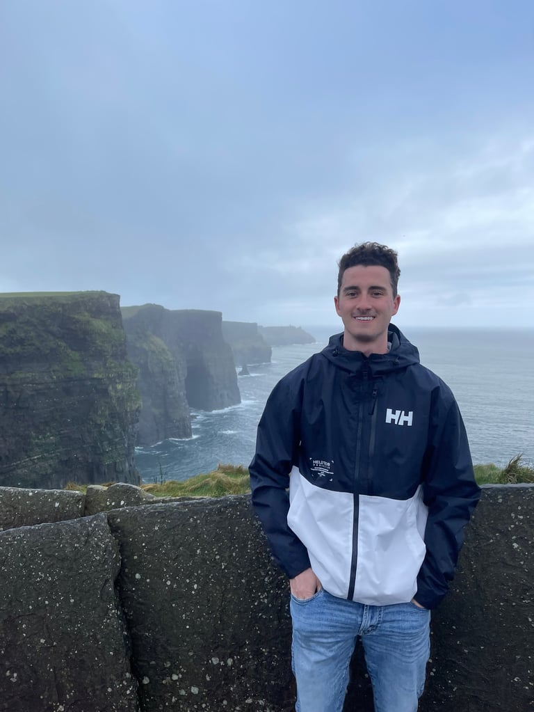 Andrew Donohue smiling at the Cliffs of Moher with the ocean in background