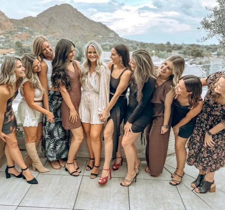 Group of women in casual summer dresses standing together on a dock with mountains and water in the background