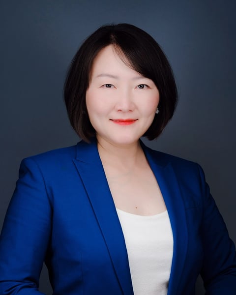 Professional headshot of an Asian woman with short dark hair wearing a blue blazer over a white top against a gray background