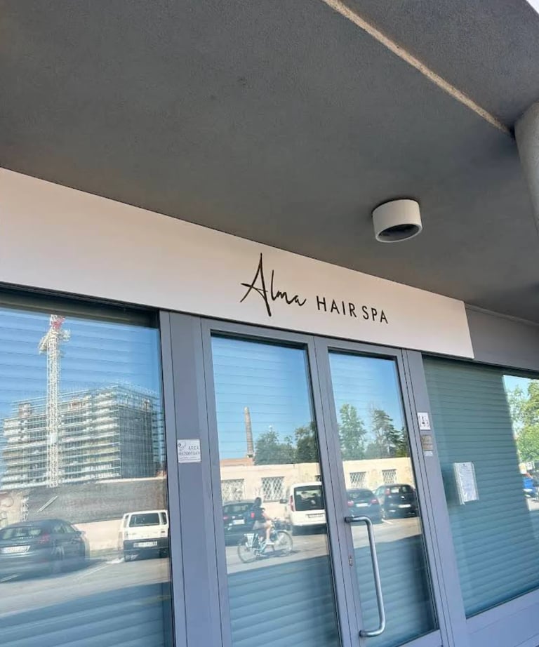 Storefront of Alm Hair Spa with glass doors and signage, reflecting city street and buildings outside