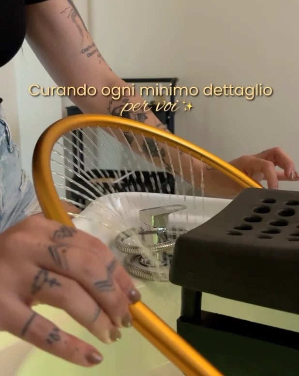 Person with tattoos holding a yellow and white electric fan, caring for every detail with Italian text overlay