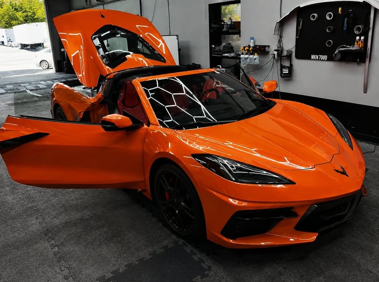 Bright orange sports car with open doors and hood displayed in a garage workshop setting